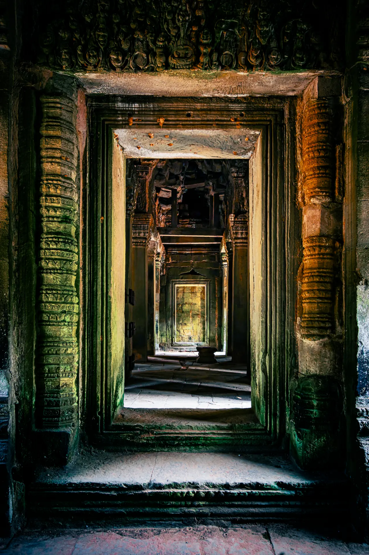 Stone corridor in Ta Nei Temple, Angkor, Cambodia. The photograph showcases a long passageway framed by ancient stone doorways and columns, with light filtering from the distant end.